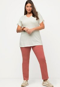 Top grigio chiaro a maniche corte con dettagli a nodo, abbinato a pantaloni corallo e sneakers beige. Il tessuto sembra morbido con una vestibilità rilassata.
