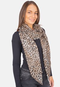 Écharpe à motifs léopard en tissu doux, avec un design fluide dans des nuances de sable et de noir, drapée autour du cou.