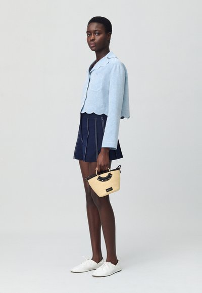 Giacca cropped azzurro chiaro con orlo scallop, gonna blu navy con righe verticali, scarpe bianche e una piccola borsa intrecciata con un accento nero.