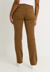 Pantalon en denim marron avec une coupe droite. Comprend des poches arrière et une taille mi-haute. Associé à des baskets blanches.