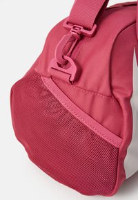 Rosa tygväska med ett texturerat nätpanel, robust rem med plastspänne och förstärkt söm.