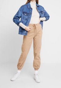 Niebieska kurtka dżinsowa z dwiema kieszeniami na piersi, założona na kremowy sweter z golfem o prążkowanej fakturze. Beżowe spodnie dresowe z elastycznymi mankietami i regulowanym pasem.