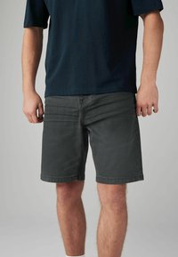 Shorts din denim gri cu croială dreaptă, dotate cu buzunare frontale și margini răsucite. Asortate cu un tricou închis la culoare, având un aspect lejer.
