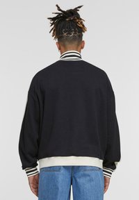 Sort sweatshirt med stribet krave og manchetter, der har en løs pasform og blød tekstur. Accentueret med en kontrastkant ved taljen.