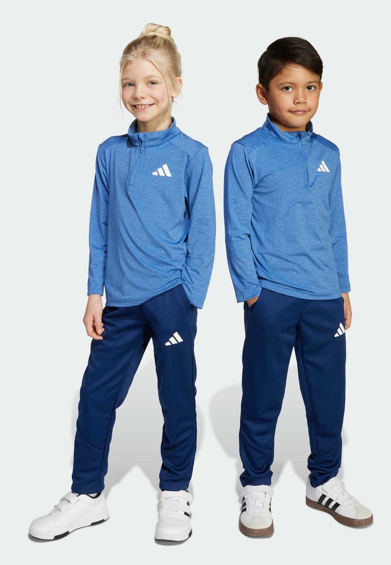 Zilas garās piedurknes sporta blūzes un tumši zilas bikses, abās ir baltas Adidas logos. Audums ir gluds; tas izskatās viegls un elpojošs.