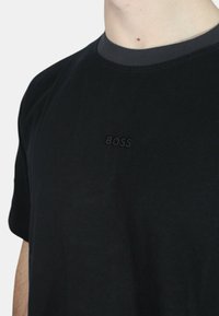 T-shirt in cotone nero con colletto rotondo, dotato di un logo "BOSS" ricamato scuro sul petto. Texture liscia e vestibilità comoda.