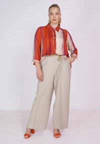 Kleurige, gestreepte blouse in tinten oranje, rood en crème, gecombineerd met beige op maat gemaakte broeken en oranje blokhakken sandalen.