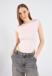 Bleda roza rebrasta bodi z rokavi na kapo in stranskimi izrezi, v kombinaciji z sivimi jeans hlačami z visokim pasom, ki imajo bleden vzorec.