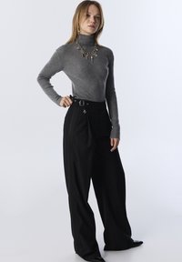 Grau gerippter Rollkragenpullover mit metallischen Glitzerpartikeln, kombiniert mit hoch taillierten, schwarzen, weiten Hosen mit Gürtel und dekorativen Hardware-Akzenten.