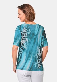 Korte mouwen top in teal en zwart met een luipaardprint ontwerp. Soepele textuur en een relaxte pasvorm, met een ronde halslijn en een gebogen onderrand.