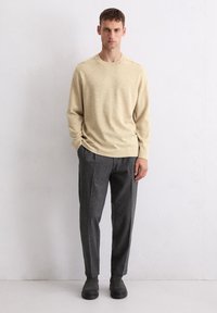 Pull en tricot beige à manches longues avec un col rond, associé à un pantalon gris ajusté et des bottines noires. Design simple, finition texturée.