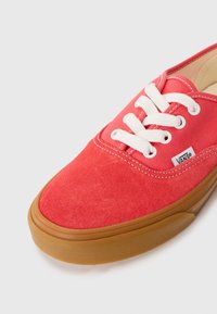 Red canvas sneaker with white laces, gum rubber sole, and VANS logo. Rounded toe and smooth texture with stitching details on the upper.