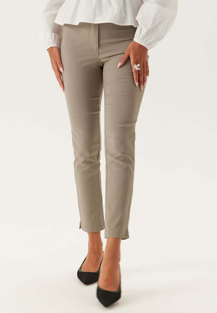 Beige slim-fit broek met een soepele textuur, voorzien van een lage taille en een cropped, gespleten zoom. Gecombineerd met zwarte puntige hakschoenen.