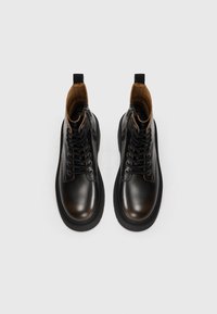 Bottines en cuir noir avec bouts ronds, lacets à l'avant, couture ton sur ton et doublure en daim marron. Dispose d'une languette à l'arrière.
