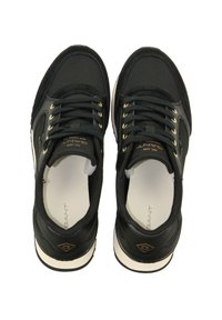 Black athletic shoes with a mesh and suede upper, featuring gold eyelets, black laces, and a white rubber sole. Notable logo detail.