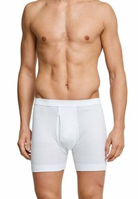 White, ribbed cotton boxer briefs with a front opening, soft waistband, and fitted design, showing the model from the waist up.