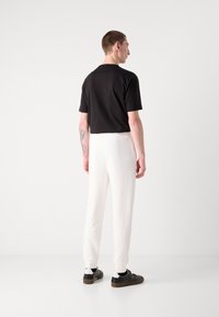 Sort kortærmet skjorte parret med hvide tapered bukser og sorte sneakers, med en glat tekstur og afslappet pasform. Bemærkelsesværdig tatovering på armen.