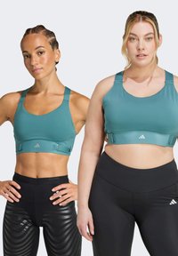 Sport-BHs aus teal-farbenem Stoff mit verstellbaren Trägern und einem Bund. Ein Paar schwarze Leggings mit strukturiertem Muster auf einer Seite und glattem Material auf der anderen.