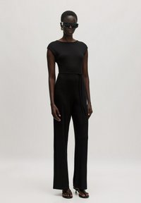 Schwarzer Rippensalerkleid mit kurzen Ärmeln, eng anliegendem Oberteil und weiter Hose. Inklusive gebundenem Taillengürtel und glänzenden schwarzen Sonnenbrille.