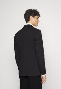 Blazer nero con taglio sartoriale, revers a punta e polsini a tre bottoni. Tessuto morbido con un design strutturato e dettagli minimi.