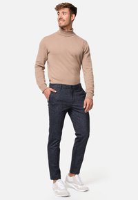 Bež turtleneck džemper u kombinaciji s tamnoplavim krojenim hlačama i bijelim tenisicama, s elegantnim dizajnom i mekim teksturama.