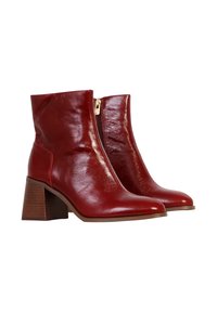 Botas de tobillo de cuero rojo con un acabado brillante, punta afilada, cremallera lateral y un tacón de madera grueso. Textura suave con acentos mínimos.