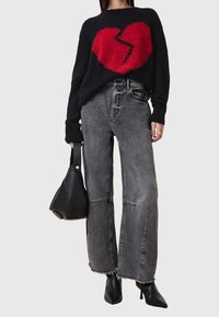 Czarny puszysty sweter z wzorem pękniętego czerwonego serca, w zestawieniu z szerokimi szarymi dżinsami i czarną torebką o fakturze. Całość dopełniają czarne szpilki.
