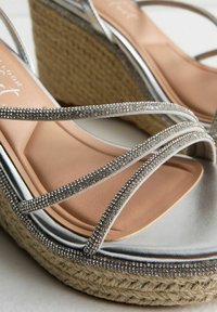 Silver wedge sandals with crisscross straps adorned with small rhinestones. Braided jute platform and soft beige footbed.