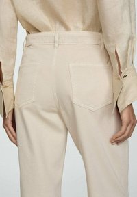 Pantaloni bej cu talie înaltă, cu croială dreaptă, având două buzunare la spate, o buclă pentru curea și o textură de țesătură netedă.