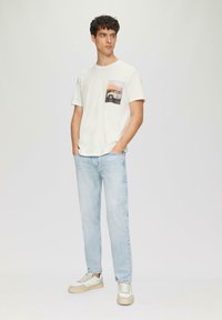 Witte katoenen T-shirt met een voorzakprint van een voertuig en zonsondergang. Gecombineerd met lichtblauwe jeans en witte sneakers.