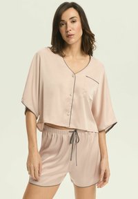 Jasnoróżowy satynowy zestaw do spania składający się z krótkiego topu z dekoltem w kształcie litery V, guzikami i kieszonką na piersi, w komplecie z dopasowanymi szortami na sznurku.