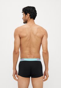 Schwarze Boxershorts mit einem hellblauen Bund, der mit pinkem "HUGO"-Branding versehen ist; hauptsächlich aus weichem Material, enganliegendes Design, minimalistischer Stil.