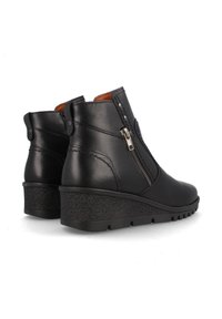 Botas de cuero negras hasta el tobillo con tacón en cuña, con cremallera lateral y costuras decorativas. Textura suave con suela de goma.