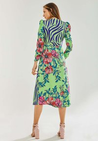 Floral and zebra-patterned dress in green, with long puffed sleeves and a mid-length A-line cut. Paired with light pink block-heeled sandals.