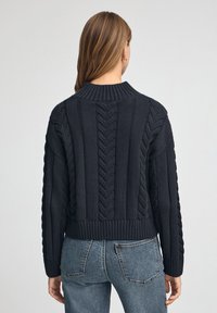 Svart stickad tröja med ett texturerat kabelmönster och ribbad nederkant. Bakdelen har en hög hals och sänkte axelsömmar.