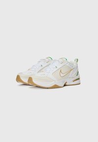 Fehér Nike sportcipők, sima bőr felsőrésszel, arany logóval, zöld kiegészítőkkel és barázdált gumitalppal.