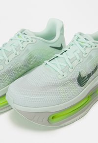 Adidași de alergare verde mentă deschis, cu plasă pe partea superioară, accente gri și pernuță de aer vizibilă în talpă. Prezintă șireturi neutre și logo.