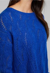 Blauer gestrickter Pullover mit Wellenmuster und offener Maschenstruktur. Abgerundeter Ausschnitt und lange Ärmel für eine legere Passform.