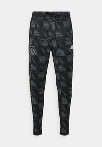 Pantalons de sport noirs avec un motif géométrique, taille élastique et rayures sur les côtés. Présente le logo Ajax et trois étoiles sur la cuisse gauche.