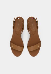 Brown sandals with a simple design, featuring a broad strap and adjustable ankle strap. Soft texture with a subtle logo accent.