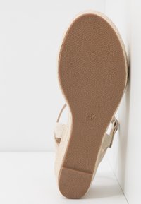 Semelle d'une sandale beige à talon compensé avec une semelle extérieure en caoutchouc brun texturé et le numéro de taille 37 visible au centre.