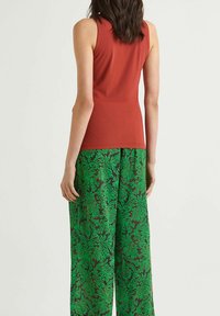 Top rosso senza maniche abbinato a pantaloni larghi verdi con un motivo floreale in diverse tonalità di verde su uno sfondo marrone.