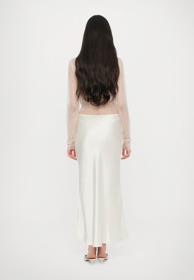 Top trasparente a maniche lunghe con motivo intricati, abbinato a una gonna in satin crema. La gonna ha una silhouette morbida e un orlo che arriva alla caviglia.