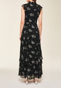 Svart blommig maxiklänning med volangärmar, lager på lager kjol och figurnära liv. Har små vita och gröna blommönster.