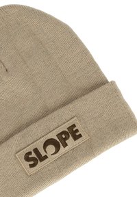 Helle beige Strickmütze mit umgeschlagenem Rand, die ein rechteckiges Patch mit dem Wort "SLOPE" in dunkelbrauner Schrift hat.