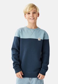 Laivastonsininen ja vaaleansininen collegepaita, jossa on värilohkodesign, resorit hihansuissa ja pääntiessä, sekä pieni merkki rinnassa.