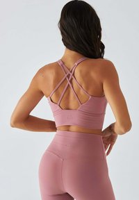 Różowy sportowy top crop z krzyżującymi się paskami na plecach, w połączeniu z dopasowanymi legginsami z wysokim stanem. Gładka faktura i dopasowany krój.