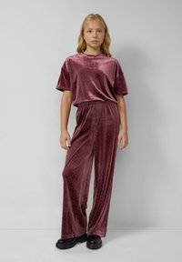 Burgundský sametový dvojdielny outfit, ktorý obsahuje voľný top s prehnutými rukávmi a široké nohavice zdobené malými kovovými nitmi.