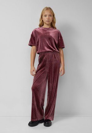 Burgundowy komplet z aksamitu składający się z luźno dopasowanej bluzki z podwiniętymi rękawami oraz spodni o szerokiej nogawce, zdobionych drobnymi metalowymi ćwiekami.
