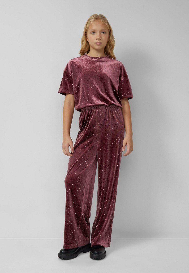 Burgundský sametový dvojdielny outfit, ktorý obsahuje voľný top s prehnutými rukávmi a široké nohavice zdobené malými kovovými nitmi.